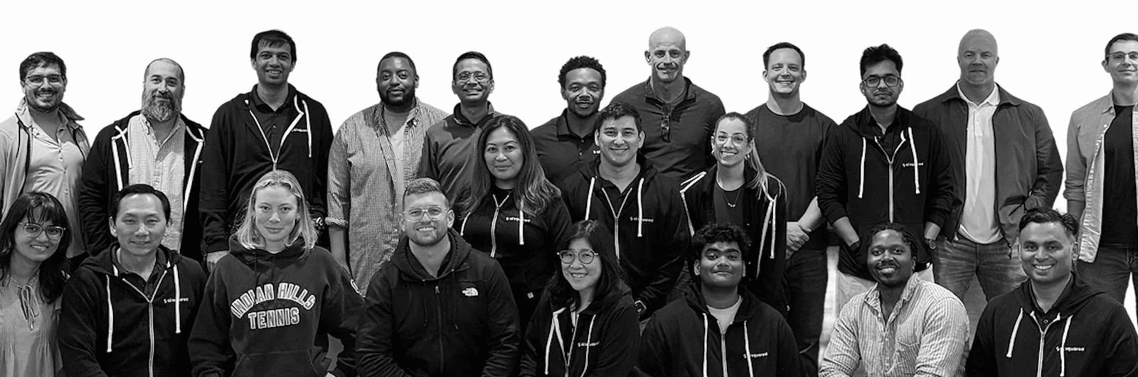 Black-and-white group portrait of the AISquared team standing and seated together on a white background